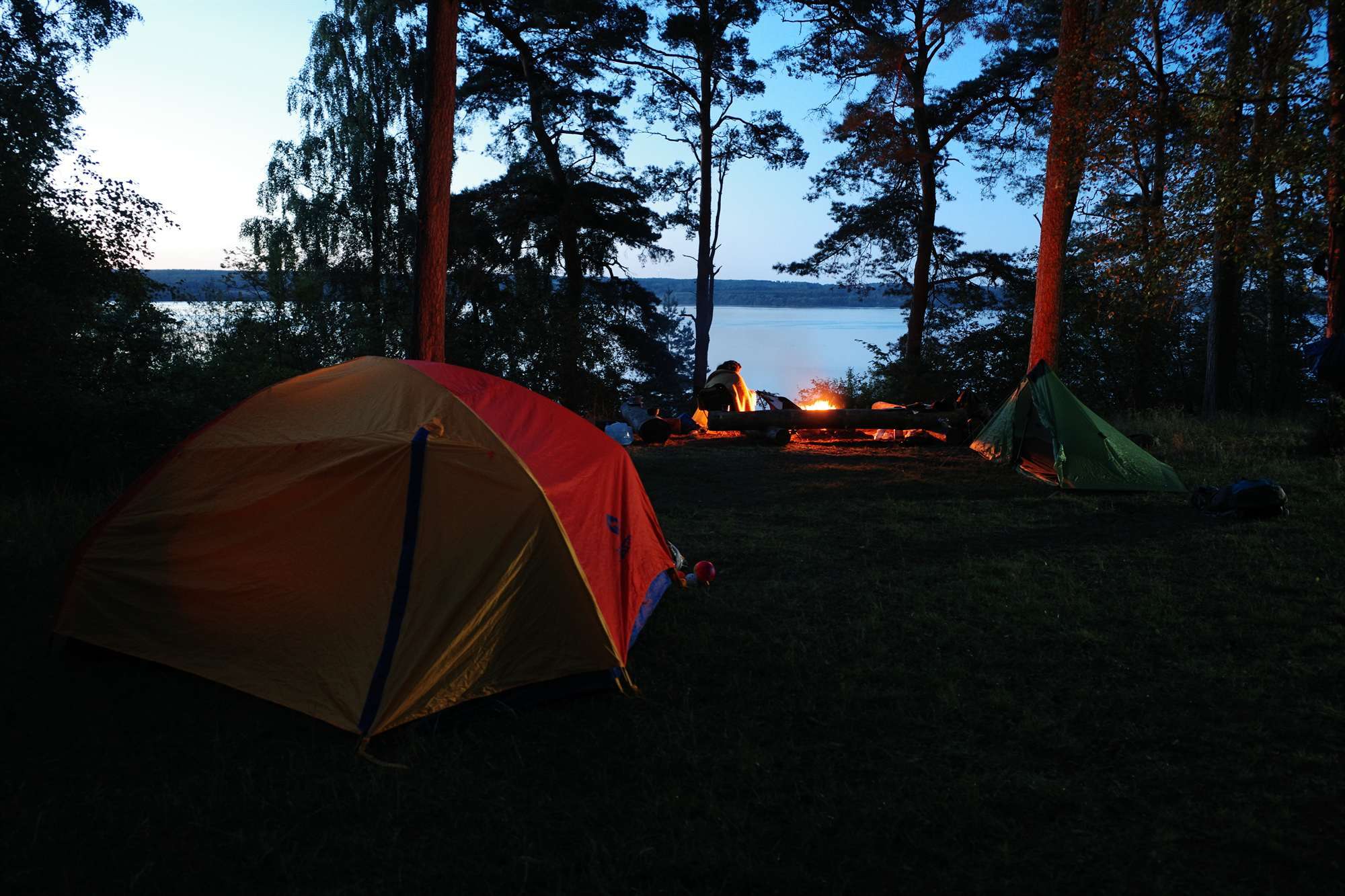 Tents and a campfire beside a lake at dusk